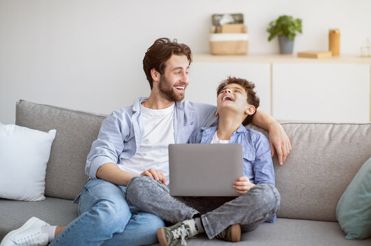 Happy dad and his son laughing, watching funny comedy on laptop at home, having fun together