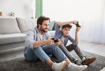 Videogames concept. Joyful father and son competing in online games, holding joysticks while...