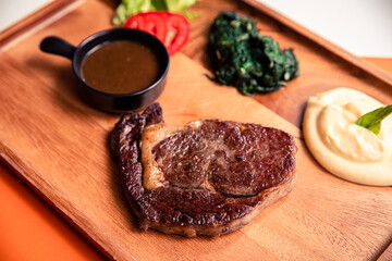 Angus beef ribeye steak with sauteed spinach, mashed potato and black pepper gravy sauce on wooden cutting board