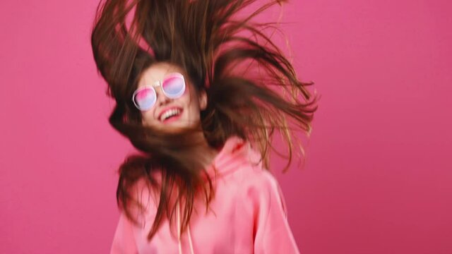 Girl teenager jumping and waving her hair in the studio on a pink background, happy smile
