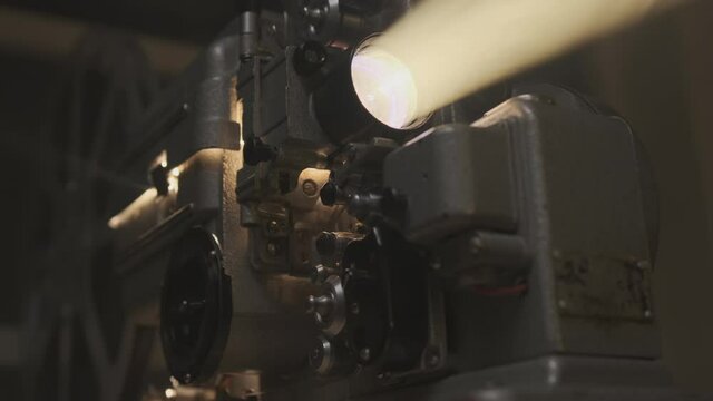 Old film projector projecting beam of light in dark room or movie theater close up.