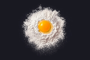 Egg in flour. Dough preparation. Black background. View from above.
