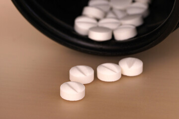 White pills on the table and a black bottle. Selective focus.