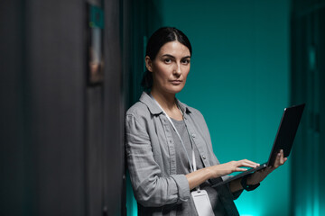 Waist up portrait of female data engineer holding laptop and looking at camera while working with...