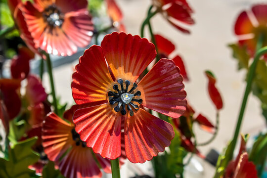 Red metal poppy lawn ornament  grainy with sand from being outdoors focused in front of other blurred metal flowers - selective focus