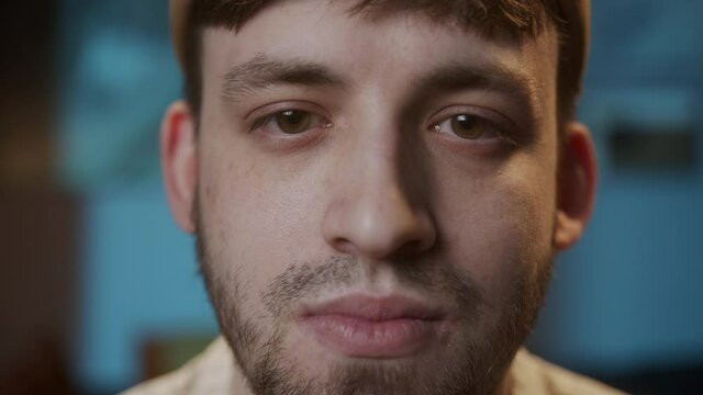 Portrait of young sad man with brown eyes, looking in camera with joyless, sorrowful view. Close-up of male face student having stubble beard.