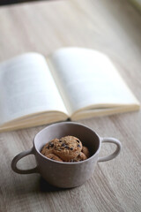 Bowl of chocolate chip cookies and open book on a table. Selective focus.