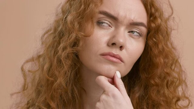 Studio portrait of thoughtful red-haired woman thinking over beige background