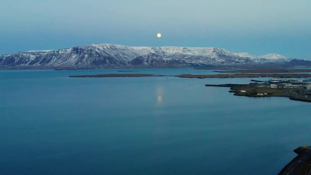 Aerial view of full moon above the sea and the Esjan mountain, on the Grotta island - tilt up, drone shot