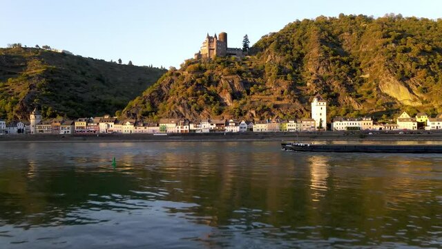 Aerial drone shot flying over the Rhine River up to Katz Castle in Germany while an industrial ship passes by.