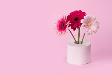 Gerbera flowers in vase made of toilet paper on pastel pink background.