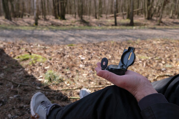 Compass on a man's palm on the background of a forest trail. Sunny day. A man sitting in the shade of a tree.