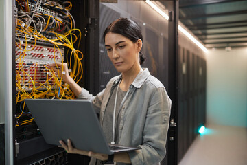 Waist up portrait of female network engineer connecting cables in server cabinet while working with...
