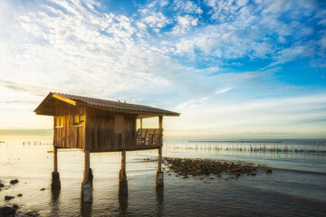Naklejka premium A small wood hut in the sea with blue sky during sunrise time.