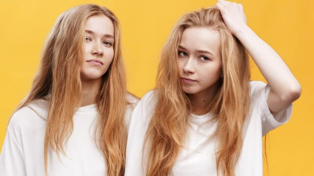 Two doubtful redhead twin sisters looking unsure, shrugging shoulders, looking uncertain, orange studio background