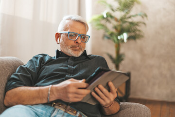 Relaxing at home with your tablet. An elderly gray-haired man watches the news on the Internet. Social networks.