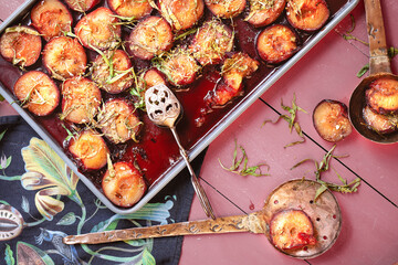 Baked plums with honey and cinnamon in a baking tray on old wood pink table with retro style spoon from above