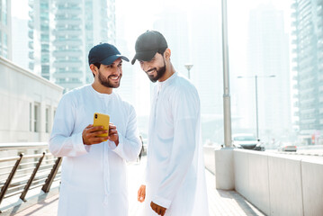 Fototapeta na wymiar Two young men going out in Dubai. Friends wearing the kandura traditional male outfit and baseball hat in Marina