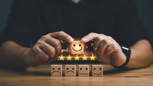 Customer service evaluation and satisfaction survey concepts. The client's hand picked the happy face smile face icon and five star symbol on wooden cube on table