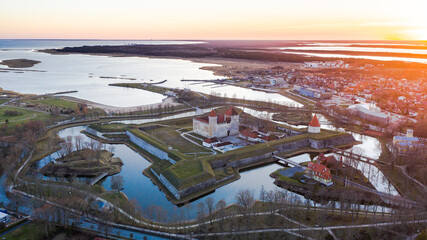 Aerial view to the sunset colored coastal historic medieval fortress with the surrounding water...
