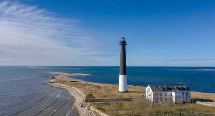 Obraz premium Aerial view to the historic lighthouse on on the daytime seascape with the long spit submerging into deep blue sea