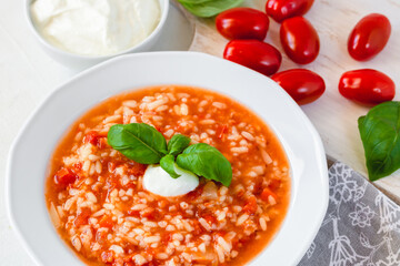 Tomato soup with rice decorated by cream and basil leaf.