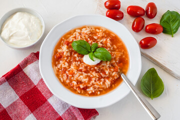 Tomato soup with rice decorated by cream and basil leaf.