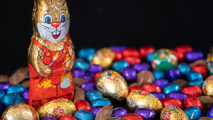 Easter bunny surrounded by multicolored eggs and chocolates, on black background