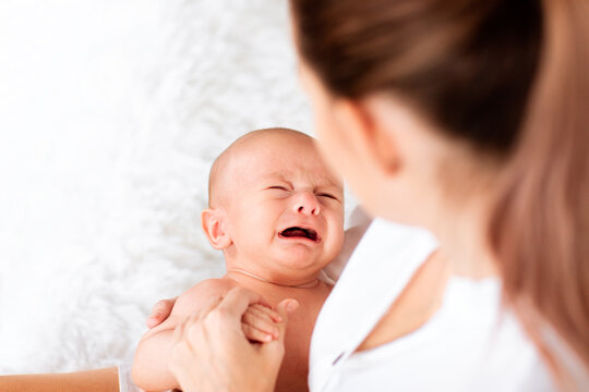 Mother with tail in white shirt holding crying newborn baby. Copy space.