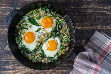 Shakshuka, fried eggs with green wild garlic leaves, onion, pepper and spices in cast iron pan, close up