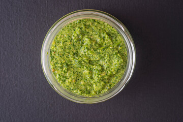 Green pesto sauce in a glass bowl isolated on black background, close up, top view