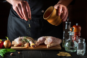The chef adds dry spices to the chicken legs. Preparation for grilling with chicken leg in the kitchen of a restaurant or cafe on table with vegetables and spices