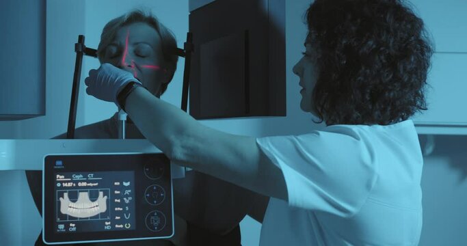 A Female Patient Standing In The 3D CBCT While A Female Medical Worker Came And Putting To The Female Patient Mouth Plastic Small Piece For Scanning A Jaw, There Is A Screen With A Human Jaw.  