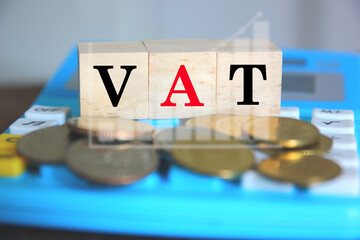 text VAT on wood cube on calculator and blur coins business graph