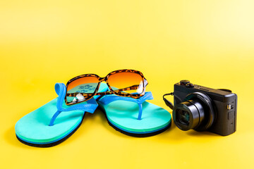 Beach slippers, flip-flops, sunglasses and a camera on the Yellow background. Summer vacation...