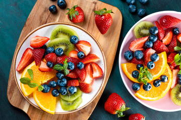 Fresh summer salad of various fruits and berries. Kiwi, orange, strawberry and blueberry on a plate decorated with mint on a blue wooden rustic background top view