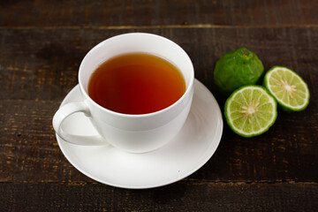 Bergamot tea or Earl Grey tea in white cup and fresh bergamot fruit with sliced on brown wooden table.