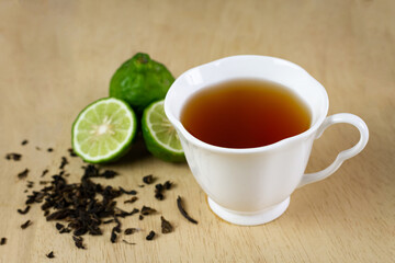 Bergamot tea or Earl Grey tea in white cup and fresh bergamot fruit with sliced on brown wooden table.