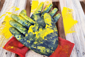 Pair of black work protective gloves painted in yellow lie on wooden pallet.