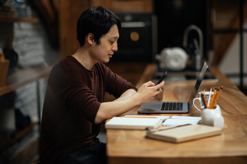Fototapeta na wymiar Asian man using smartphone while working at home