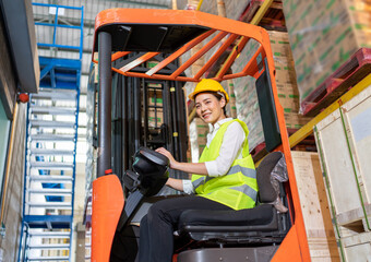 Forklift driver asian young woman in safety jumpsuit uniform with yellow hardhat at warehouse....