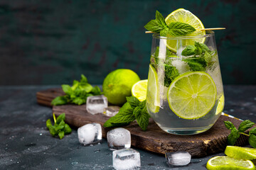 Refreshing mojito with lime, mint and ice in a glass on a dark background, free space for text. Cold summer cocktail