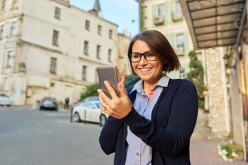 Fototapeta premium Middle-aged business woman in in cardigan glasses with mobile phone