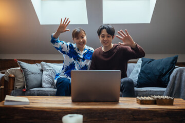 Asian couple having video call in the living room and waving