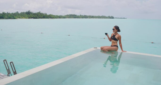 Travel luxury concept. Woman drinking coffee cappuccino relaxing wearing bikini in infinty pool looking at view of ocean. Travel vacation Luxury living at resort or expensive private villa. Bora Bora