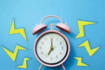 Ringing pastel pink alarm clock on blue background with yellow lightnings. Setting off the alarm. A concept stock photo for deadlines, waking up early in the morning and running out of time