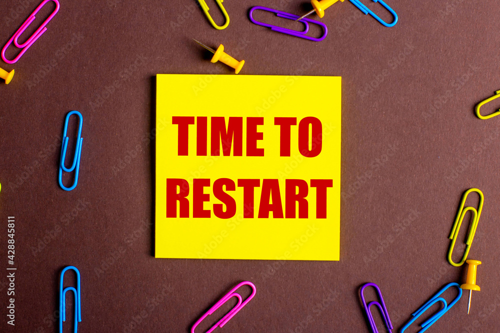Poster the words time to restart is written in red on a yellow sticker on a brown background next to multi-