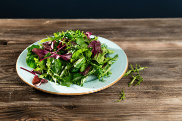 salad mix of fresh herbs, arugula, Swiss chard, spinach in tarenle on a wooden background, top-side view