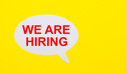 On a bright yellow background, white paper with the words WE ARE HIRING