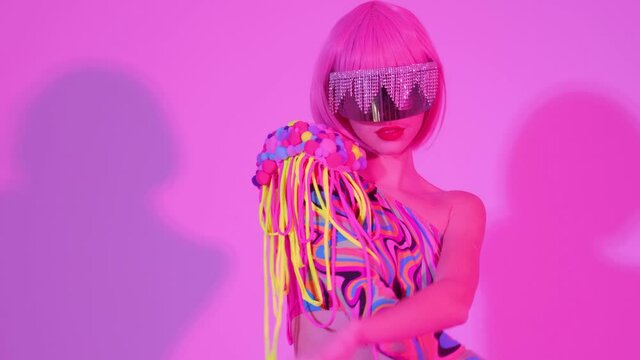 Portrait of a girl in creative glasses in pink trendy neon light. The woman dances and moves gracefully to the club music.
